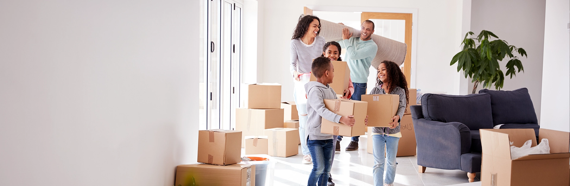 Family of five carrying moving boxes in living room